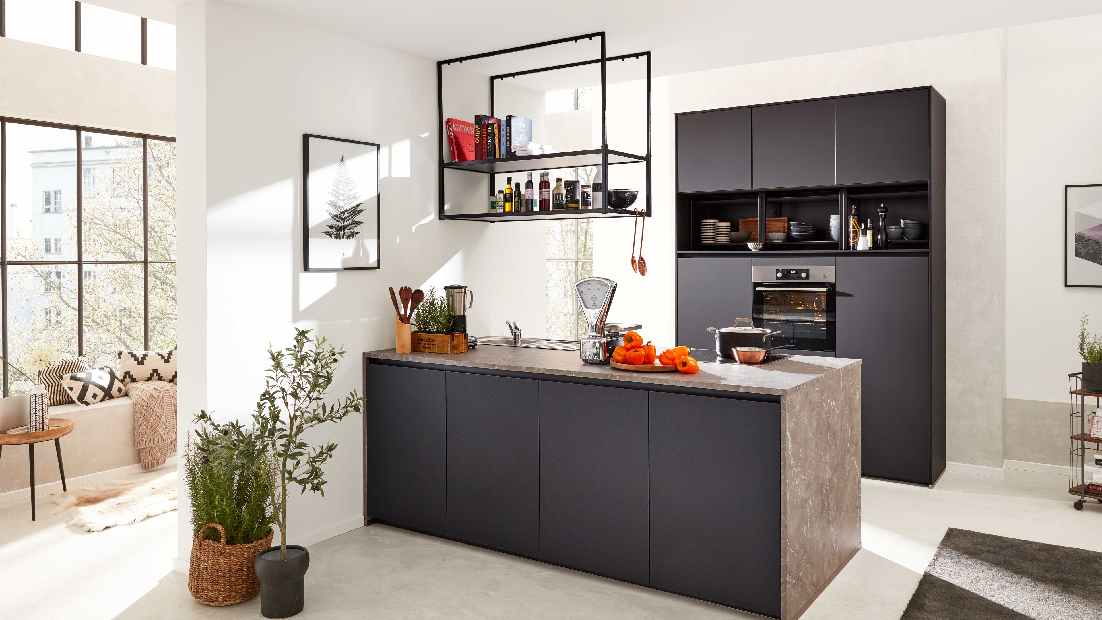 Schwarze Kücheninsel mit Marmorarbeitsplatte, hängendem Metallregal, Hochschrank mit Backofen, Waage und orangefarbenen Früchten.