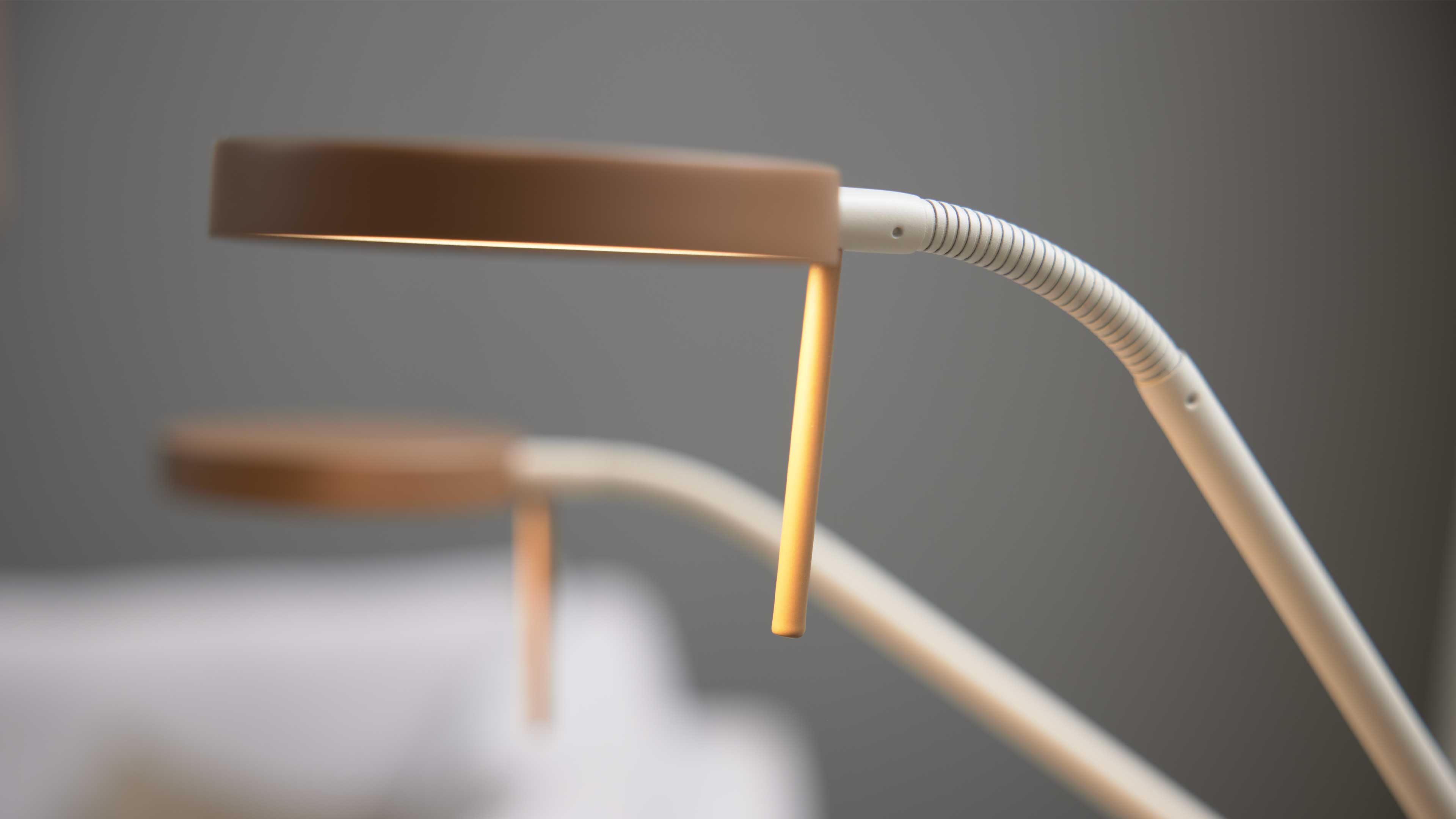 Zwei Tischlampen mit runden Köpfen, leuchtenden dünnen Stäben und weißen flexiblen Armen vor diffusem, grauem Hintergrund.