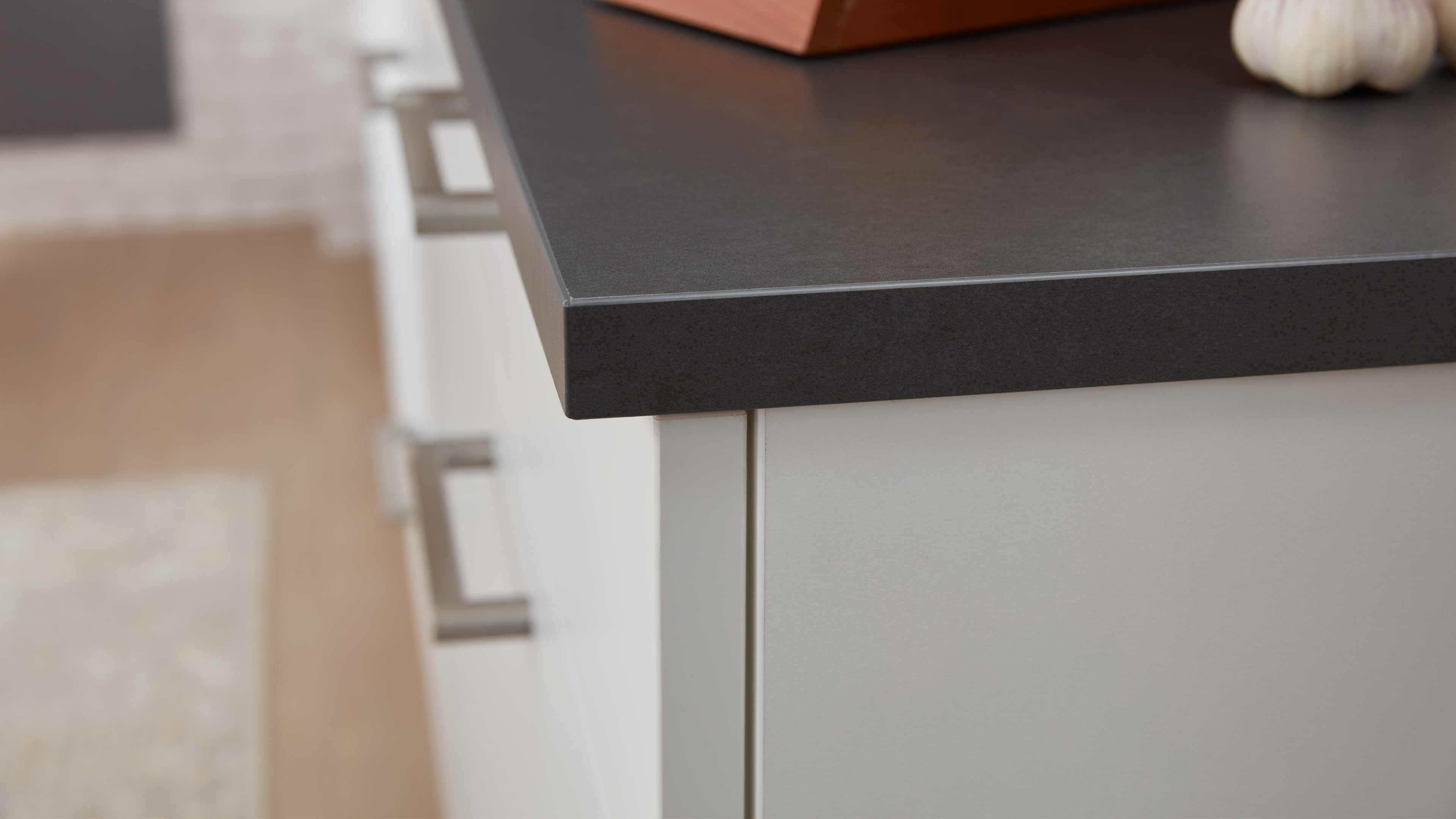Dunkelgraue, matte Küchenarbeitsplatte mit schmaler Kante über weißen Schrankfronten und Metallgriffen.