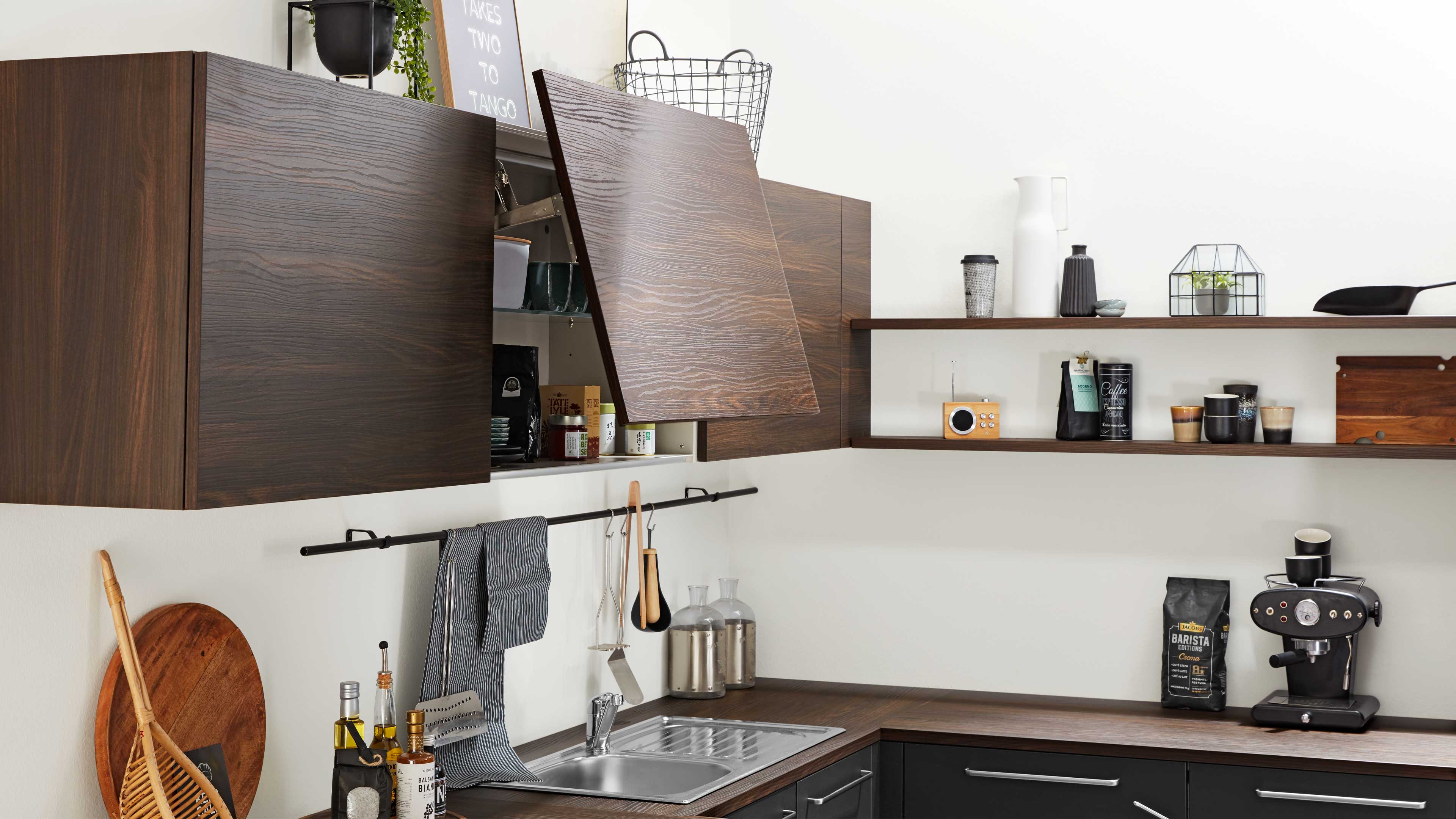 Dunkle hängende Holz-Küchenschränke, eine Klapptür geöffnet über der Spüle, offene Regale mit Kaffeebehältern und Espresso-Maschine.