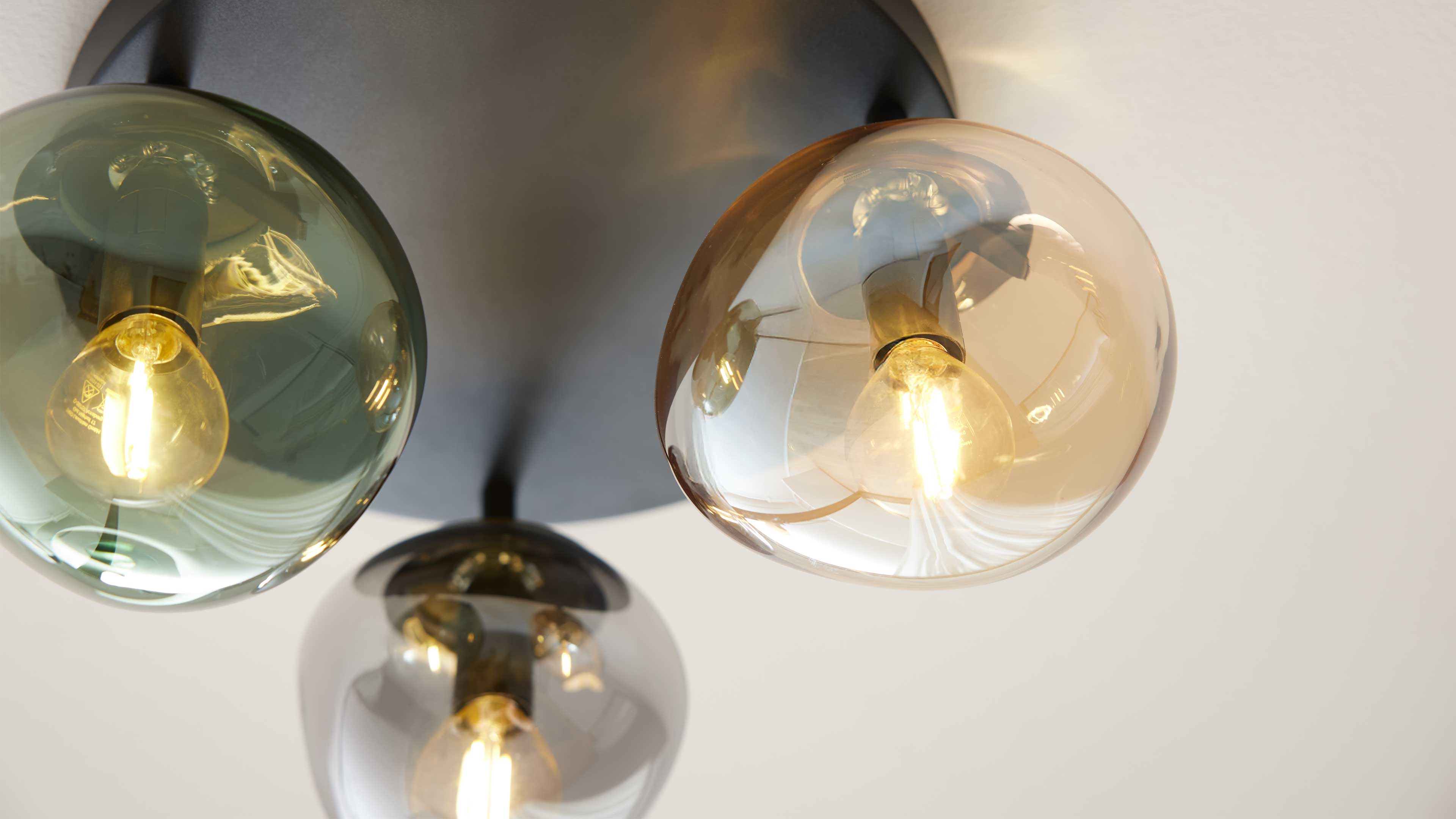 Dreiflammige Deckenleuchte mit drei farbigen Glasglocken (grün, bernstein, rauchgrau) und klar sichtbaren Leuchtmitteln.