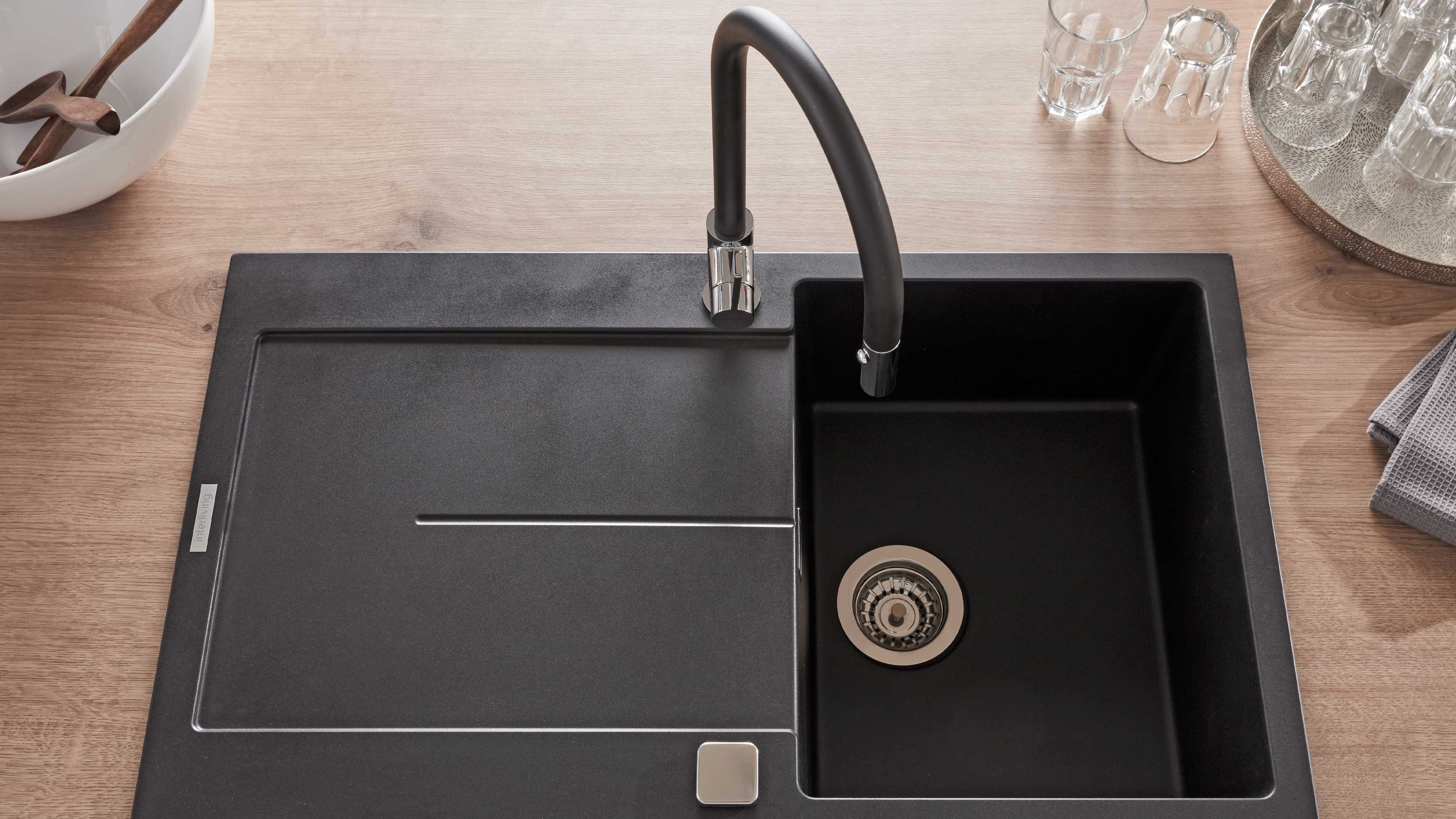 Schwarze Einbauspüle mit großem rechteckigem Becken rechts, integrierter linker Abtropffläche und hoher schwarzer Armatur mit Chromfuß.