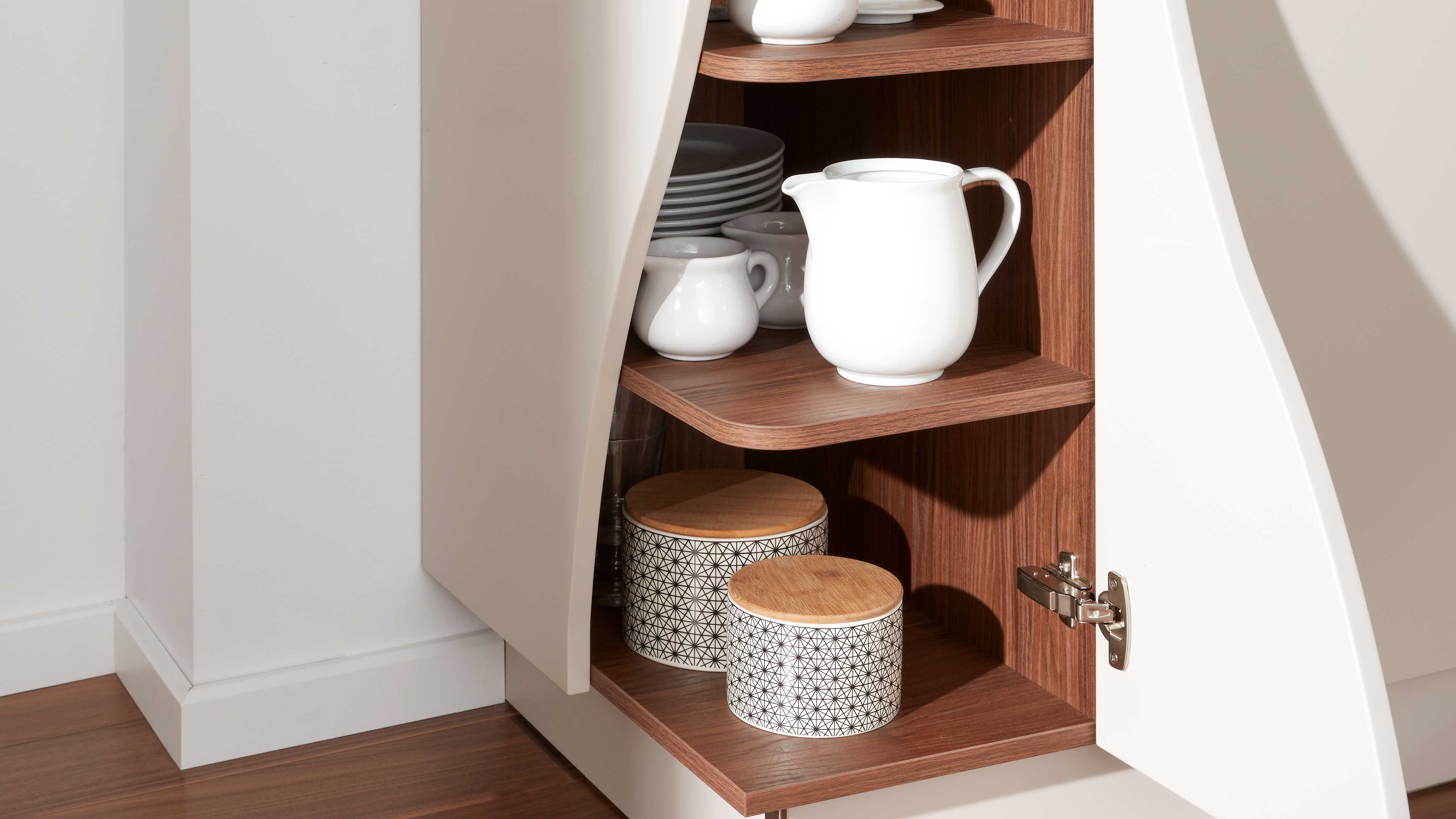 Offenes Küchenregal mit weiß lackierter Tür und Holzinnenraum, mit weißem Geschirr und zwei gemusterten Vorratsdosen mit Holzdeckeln.