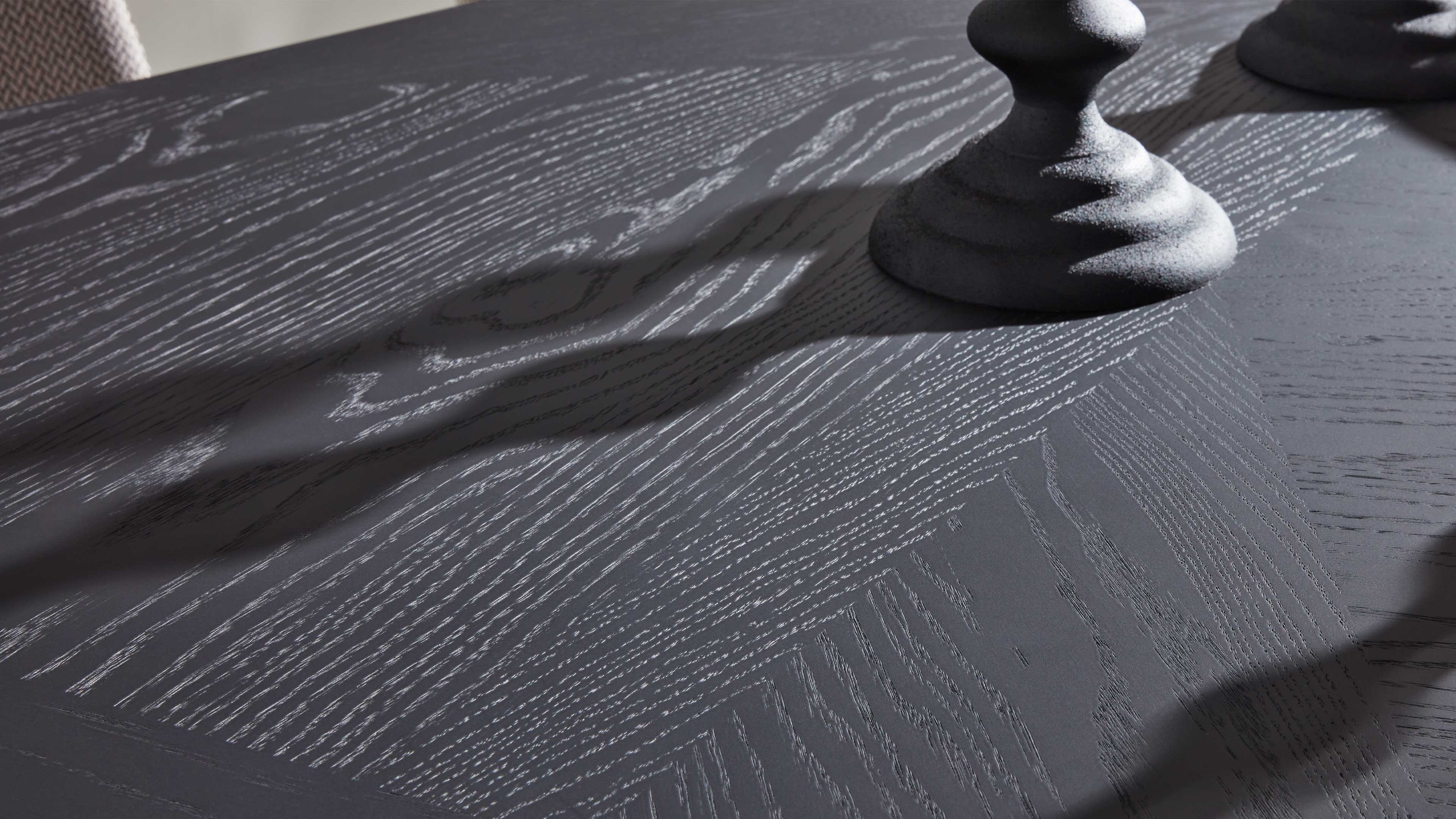 Dunkle Tischplatte mit ausgeprägter Holzmaserung, dazu zwei runde, strukturierte Objekte und Schatten.