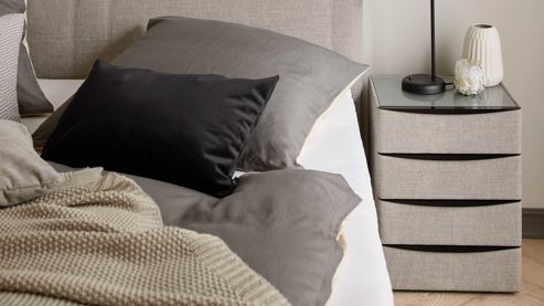 Nachtkommode Interliving aus Holz in Grau Interliving Boxspringbett Serie 1401 – Nachtkommode silberfarbener Stoffbezug Rob 533006 – vier Schubladen